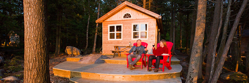 A couple sits in front of a cabin in the woods. 