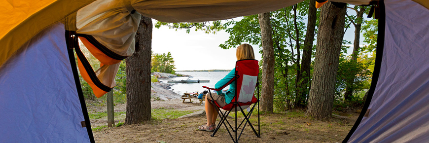 View out of a tent door showing a women sitting on a chair near the water.