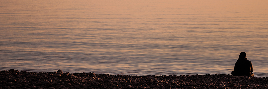 Assise sur une plage de galets, une personne regarde la vaste étendue d’un lac Supérieur calme au crépuscule.
