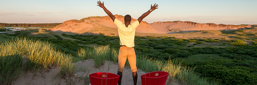 Man standing by red chairs in PEI National Park with arms outstretched.