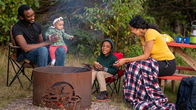 Famille de quatre personnes assises autour d'un feu de camp dans un terrain de camping.