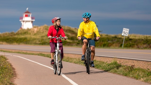 Two cyclists on a pathway in front of a lighthouse.