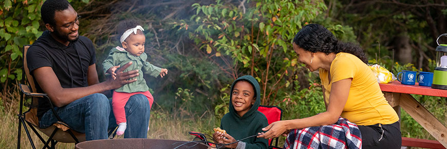 Une famille souriante de quatre personnes est assise autour d'un feu de camp enfumé dans un camping de Stanhope. 