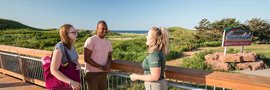 A Parks Canada guide stands chatting to two visitors at the Cavendish Dune Crossing in PEI National Park. 