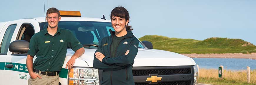 Deux membres du personnel du parc national de l'Î.-P.-É. sont souriants et se tiennent devant un camion de Parcs Canada à Covehead. 