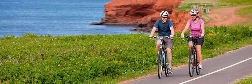 Colour photo of man and woman cycling in PEI National Park along the water.
