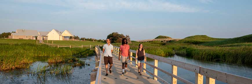 Trois jeunes marchent sur le Cavendish Dunelands Trail, avec la plage et les installations de Cavendish en arrière-plan. 