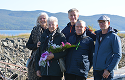 Une dame âgée avec une gerbe de fleurs dans les bras est entourée de sa famille