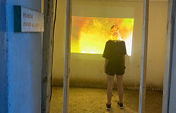 Dans un tunnel, une jeune femme de dos regarde un rectangle lumineux au mur.