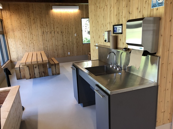 L'intérieur d'un de bâtiments de service du camping Des-Rosiers, avec table adaptée pour personne à mobilité réduite et lavabo.