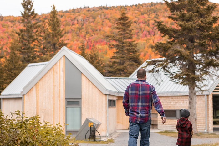 A father and son walk toward one of the service buildings at Petit-Gaspé campground. In the background, the colourful fall mountains can be seen.
