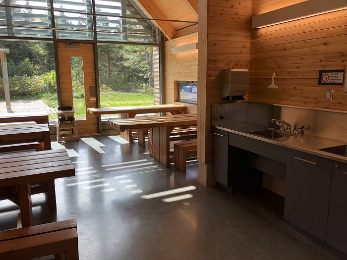 L'intérieur d'un des bâtiments de service du camping Petit-Gaspé, avec tables adaptées pour personnes à mobilité réduite et un lavabo.