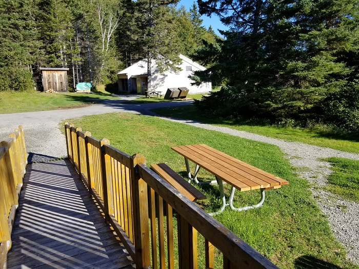 The access ramp and the table adapted for people with reduced mobility of the oTENTik F2 tent at Petit-Gaspé campground. In the background you can see the service building of Loop F. 