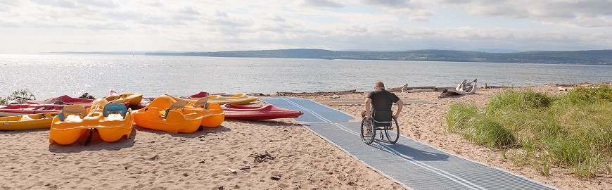 Un homme en fauteuil roulant à la plage de Penouille se dirige vers la mer sur un tapis universel déposé sur le sable.