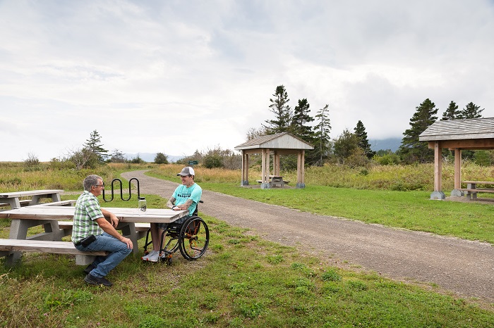 Two men, one in a wheelchair, sit at a picnic table adapted for people with reduced mobility along the Du Banc trail.