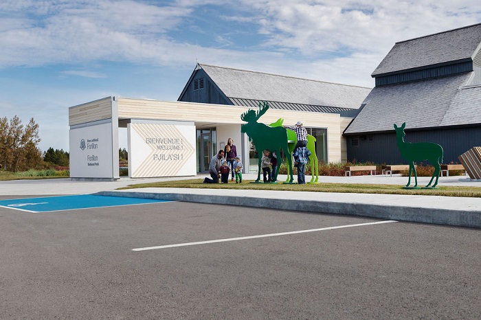 Part of the parking lot and the Visitor Information and Discovery Centre building. Visitors play near the decorative animal silhouettes.