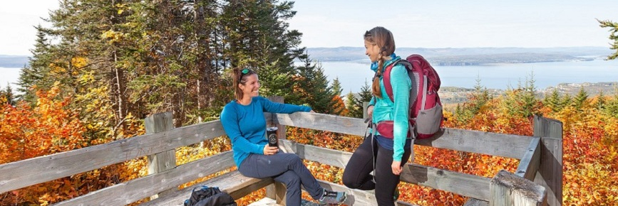 Two women admire the autumn landscape at the belvedere on the Les Crêtes trail. You can see Gaspé Bay further down.