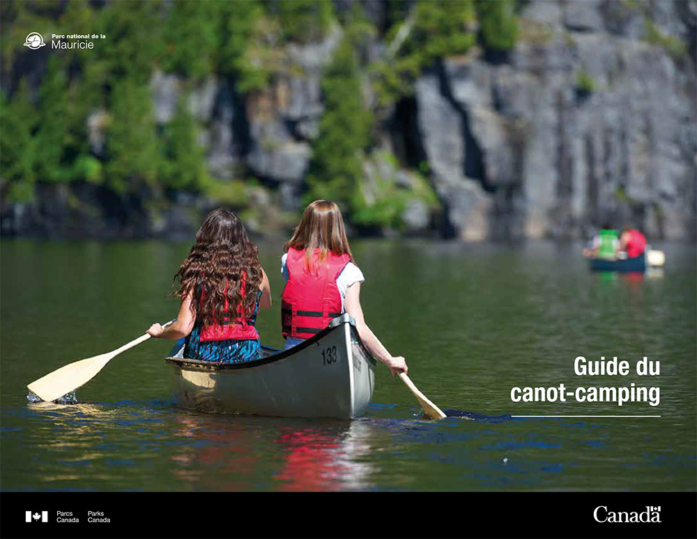 Couverture du guide de canot-camping 2023 en version française - deux jeunes canoteuses de dos pagayant sur un lac calme
