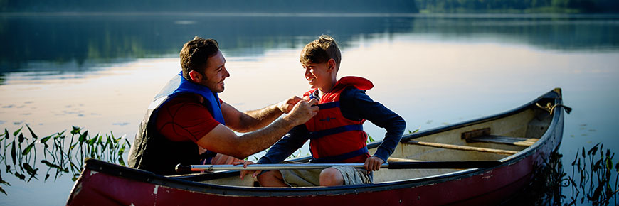 Father fastening the life jacket of his son in a canoe