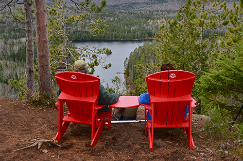 A couple sitting on red chairs in front of a forest landscape