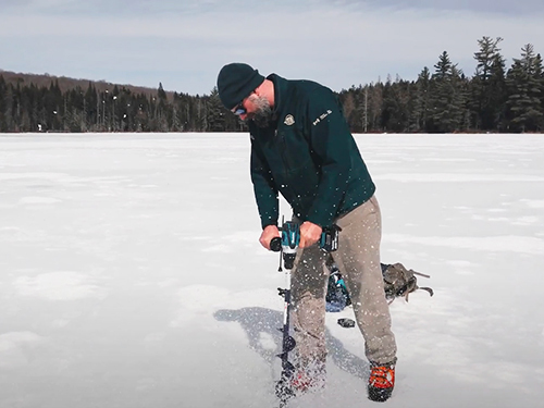 Un travailleur de Parcs Canada creuse un trou sur dans la glace sur un lac