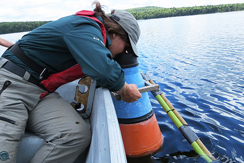 À bord d’une embarcation, une employée de Parcs Canada regarde sous l’eau à l’aide d’un appareil spécialisé.