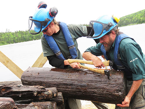Two Parks Canada employees remove a log from the bottom of a lake