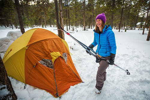 Une femme tenant des ski de fond sourit devant sa tente