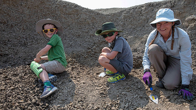 Two boys dig for fossils with the palaeontologist.