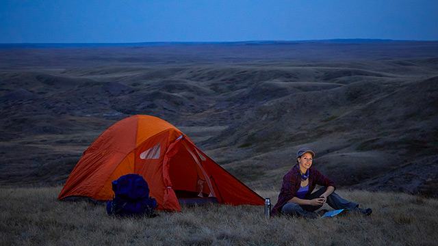 A backcountry camper sitting outside her tent in the West Block of Grasslands National Park.