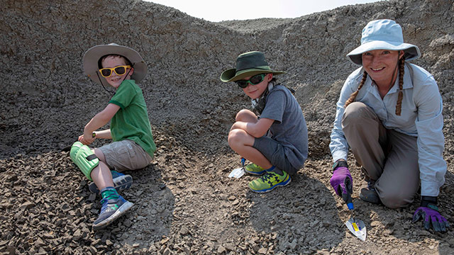 Deux garçons creusent à la recherche de fossiles en compagnie du paléontologue.