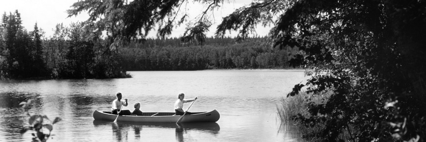Three adults paddle in a canoe across a still lake surrounded by trees