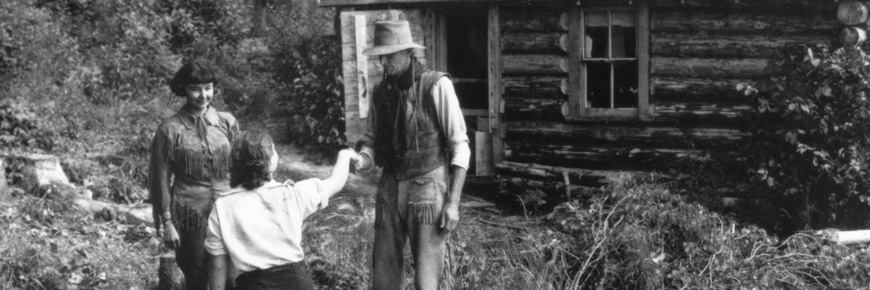 historical photograph of two people, Gertrude Bernard and Archibald Belaney, welcoming a woman to a cabin.