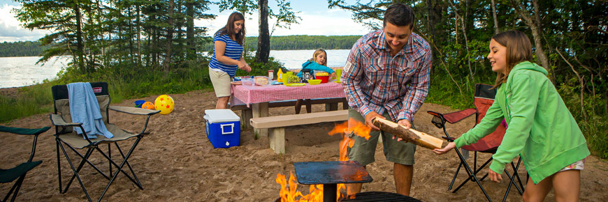 Une fillette aide son père à alimenter un feu pendant que sa sœur et sa mère préparent un pique nique.