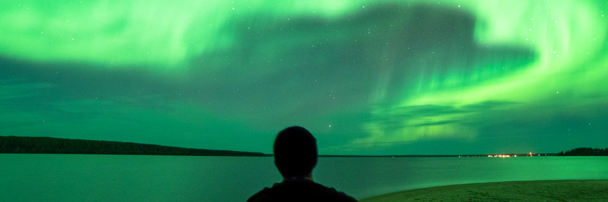 A man’s shoulders and head are silhouetted by the northern lights as he gazes at the night sky.