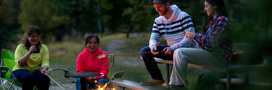 A group of four young adults enjoy roasting marshmallows around a campfire.