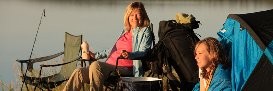 A women and her daughter enjoy the morning sunrise from their lakeside campsite. 