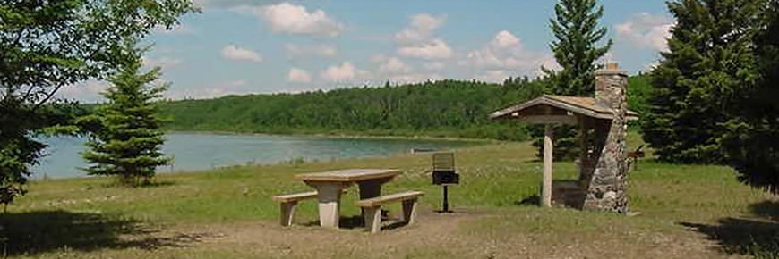 A scenic image of a lakeside picnic site featuring a stone fire place. 