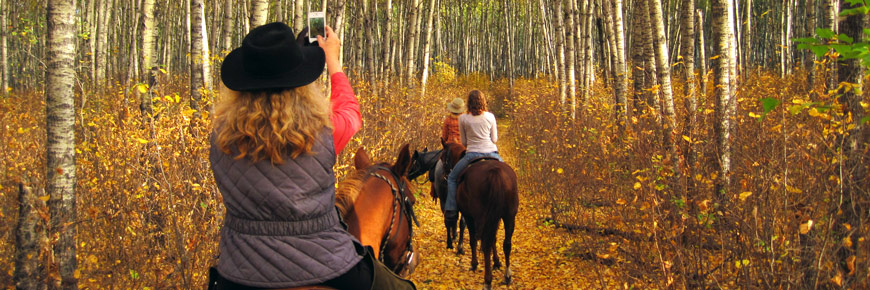 A woman on horseback pauses on the trail to take a photo of other riders.  