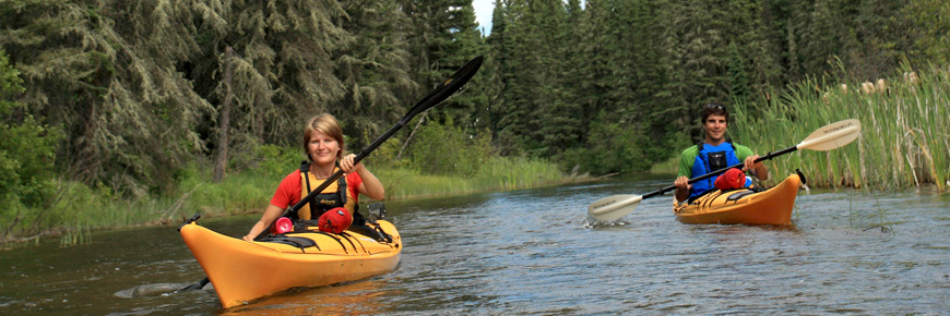 A man and a women paddle kayaks against the current in a small river. 