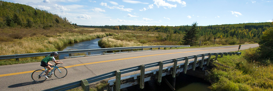 Un cycliste sur route traverse un pont qui franchit une petite rivière.