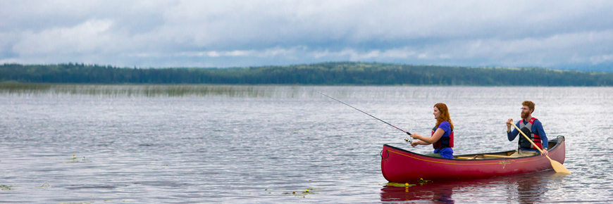 Dans un canot, un homme pagaie pendant qu’une femme pêche à l’avant.
