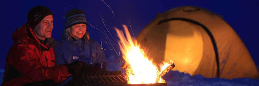 Un homme et une femme se réchauffent près d’un feu de camp à côté de leur tente par une froide soirée d’hiver.