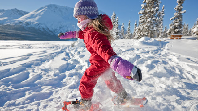 A child running in the snow and wearing snowshoes