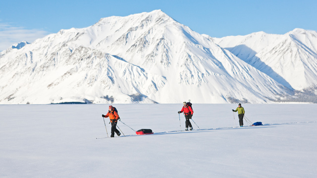 Three people cross country skiing across a snowy lake