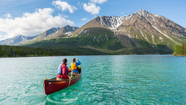 Des gens pagayent dans un canoë sur un lac bleu et une montagne devant eux