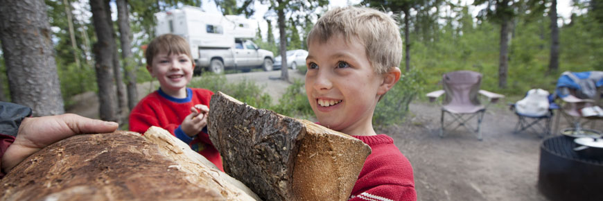 two boys carrying firewood at a campsite