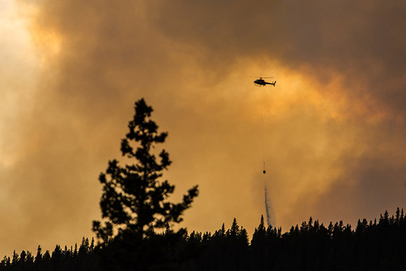 Un hélicoptère utilise des seaux d'eau pour combattre un feu de forêt dans le Parc 