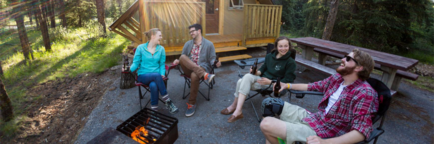 Quatre campeurs sont assis autour d’un feu devant une tente oTENTik.