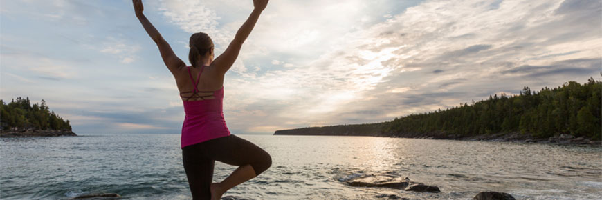Une femme pratique le yoga sur une plage au lever du soleil.